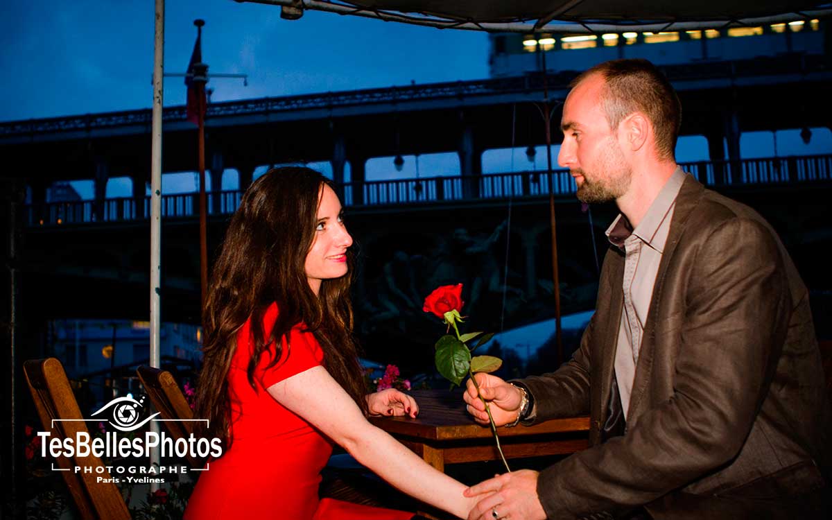 Photo demande en mariage romantique avec une branche fleur rose dans la nuit bleue sur une péniche sous le Pont de Bir-Hakeim à Paris, Love Session demande en mariage originale Paris